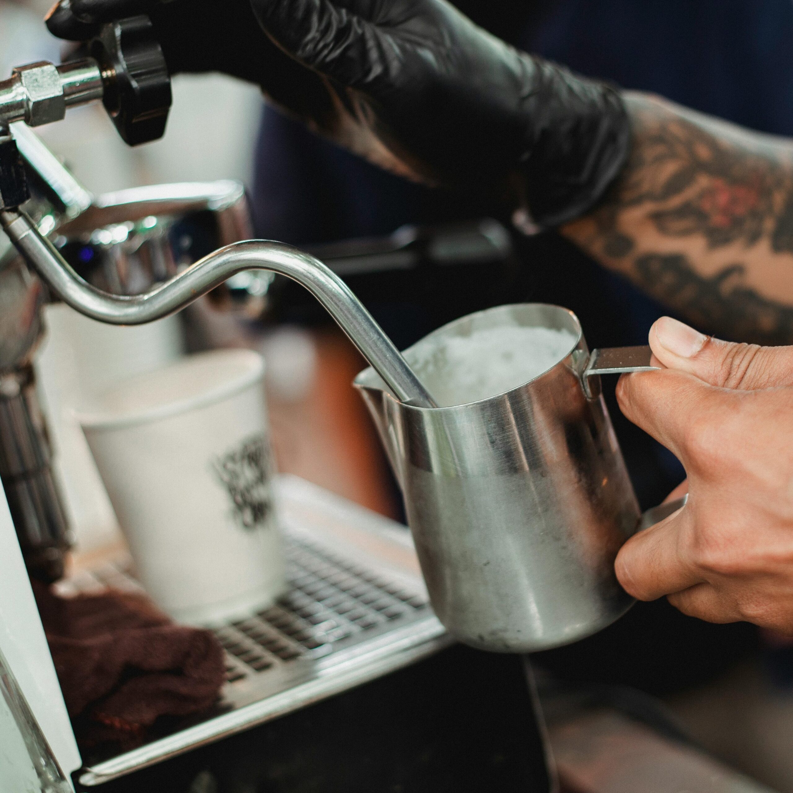 Crop faceless barista frothing milk with steam wand